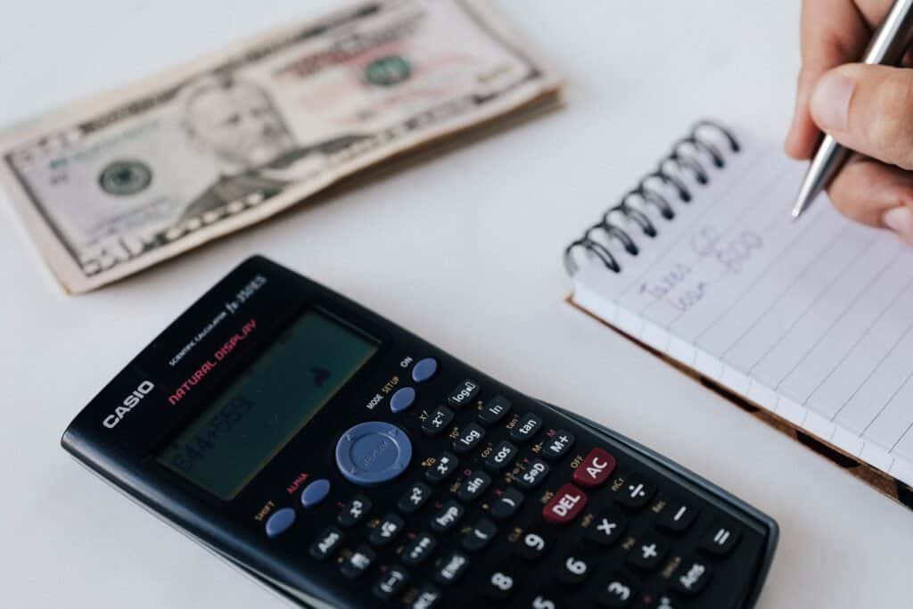 Calculator, US dollar bill and notebook used to work out the total O-1 visa cost