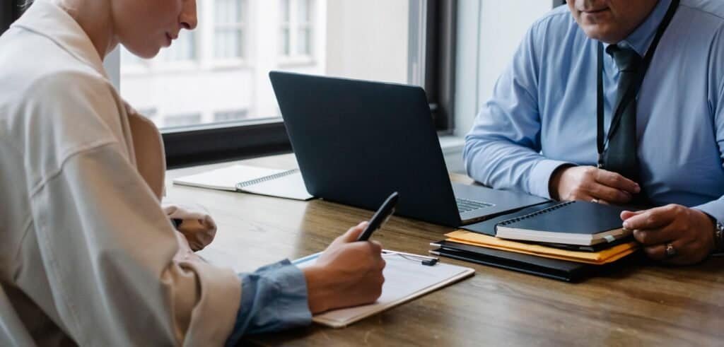 Two professionals signing contract documents at an office desk, illustrating the O-1 visa agent vs. employer sponsor petition structure