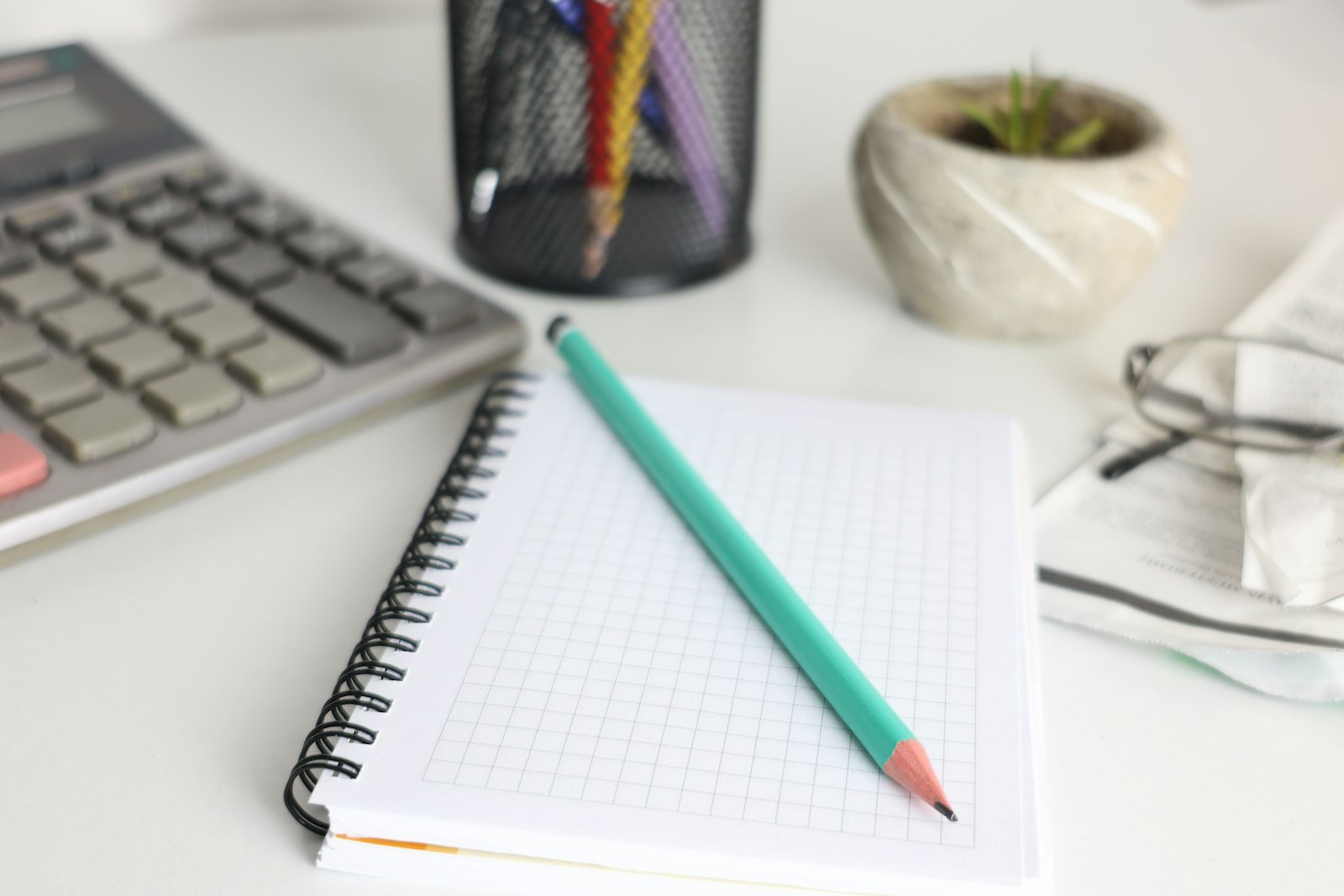 Desk with a calculator, notebook, pencil, and plant for budgeting EB-1A green card costs